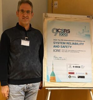 Mahdi Dibaei next to the advertising poster for the conference