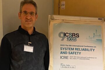 Mahdi Dibaei next to the advertising poster for the conference